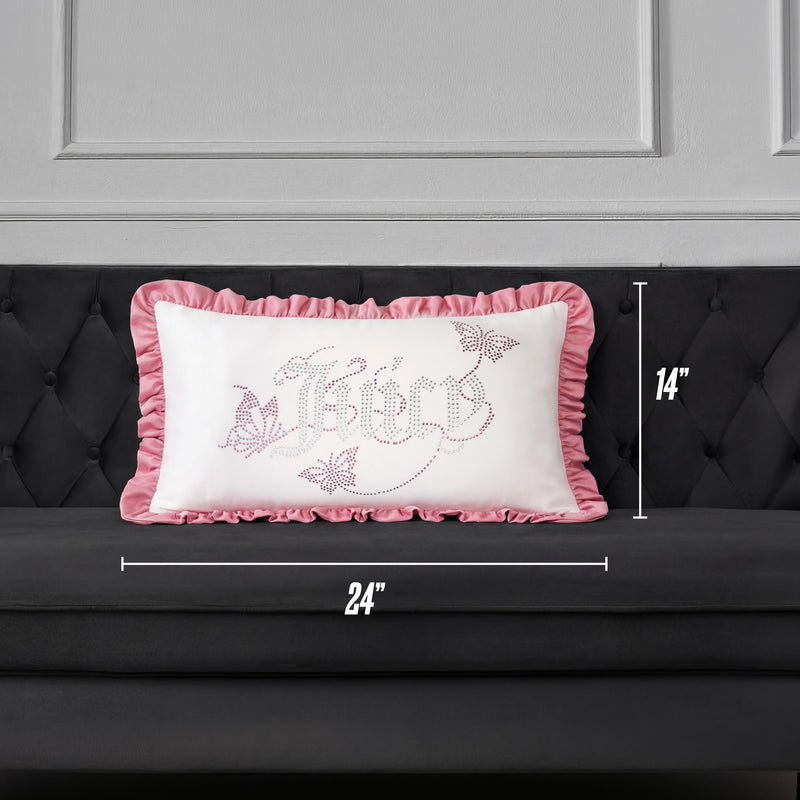 A Ruffle Decorative Pillow by Juicy Couture, featuring pink ruffled edges and a decorative design, is placed on a dark gray couch. This rectangular pillow measures 24 inches wide by 14 inches tall.