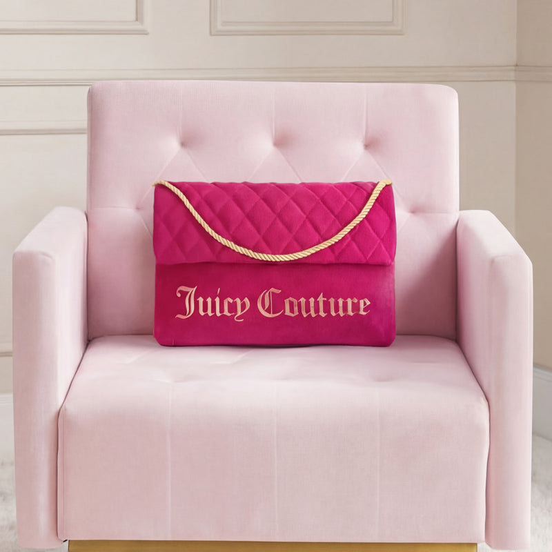A Purse Decorative Pillow is paired with a bright pink Juicy Couture quilted bag on a pale pink armchair, set against a neutral paneled wall for a trendy accent.