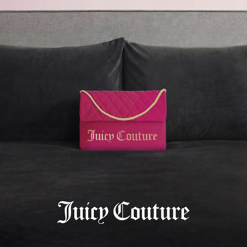 The Purse Decorative Pillow, styled like a pink quilted Juicy Couture handbag with a gold chain and logo, adds a trendy accent to any dark gray velvet couch. "Juicy Couture" is displayed in white text below.