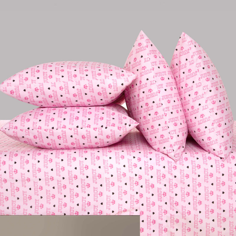 Four pink pillows and the "Microfiber Sheet Set With Extra Pillowcases," featuring an ultra-soft microfiber fabric adorned with a repeating pattern of hearts and the word "love" in red and purple, are arranged neatly on a bed against a plain gray background—creating the signature style of Juicy Couture bedding.