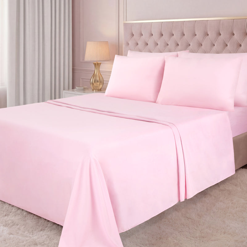 A neatly made bed with a light pink Microfiber Sheet Set With Extra Pillowcases, a tufted beige headboard, a white nightstand with a gold lamp, light curtains, and a white shaggy rug in a softly lit bedroom create an inviting atmosphere of luxury bedding.