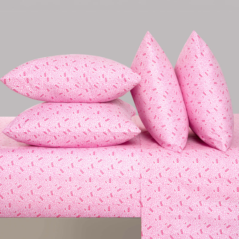 Four pink pillows with a small, repeating pattern are stacked and propped up on a matching Microfiber Sheet Set With Extra Pillowcases, all set against a plain light gray background for a touch of luxury bedding perfection.