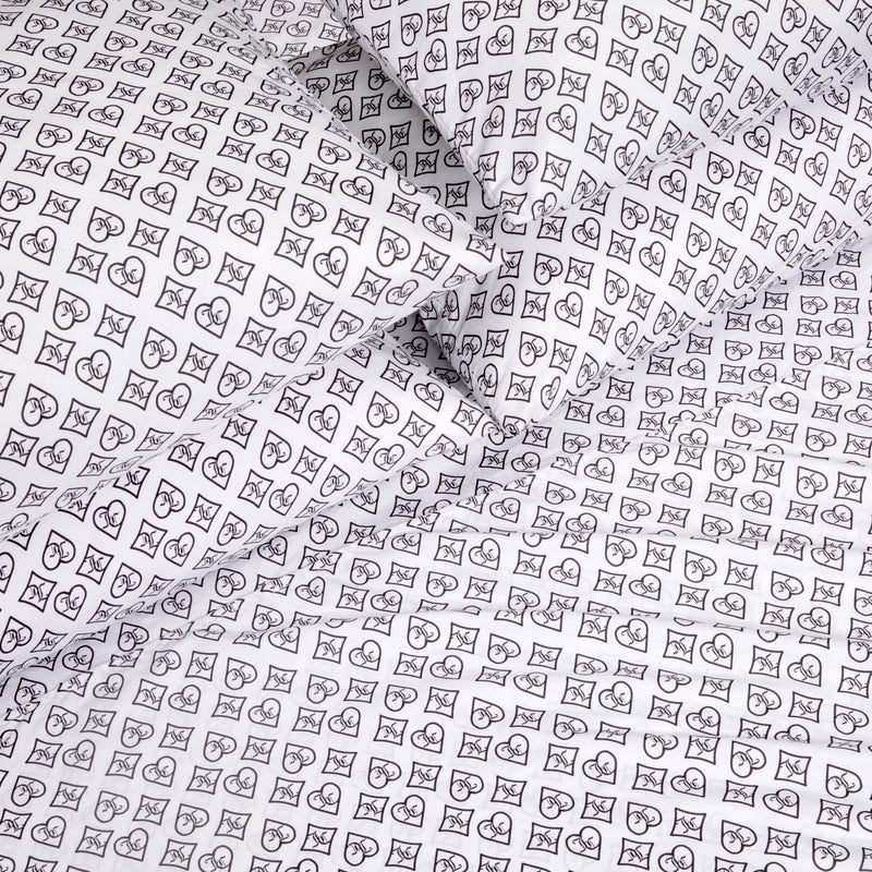 The Microfiber Sheet Set With Extra Pillowcases showcases white luxury bedding adorned with a black outlined pattern of hearts, crescent moons, and stars arranged in small square grids, elegantly covering multiple pillows and sheets.
