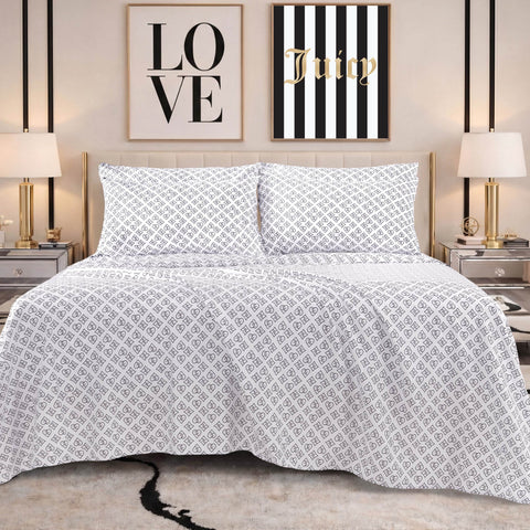A neatly made bed with a white and gray geometric patterned quilt is flanked by two nightstands with lamps. The bed features a luxury bedding ensemble, complemented by the Microfiber Sheet Set With Extra Pillowcases for added comfort. Above the bed, two framed art pieces reading "LOVE" and "Juicy" adorn the wall.