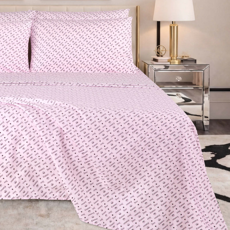 A neatly made bed with a pale pink Microfiber Sheet Set With Extra Pillowcases, featuring a small repeating black pattern, is situated next to a mirrored nightstand with a gold lamp and books in a modern bedroom setting.