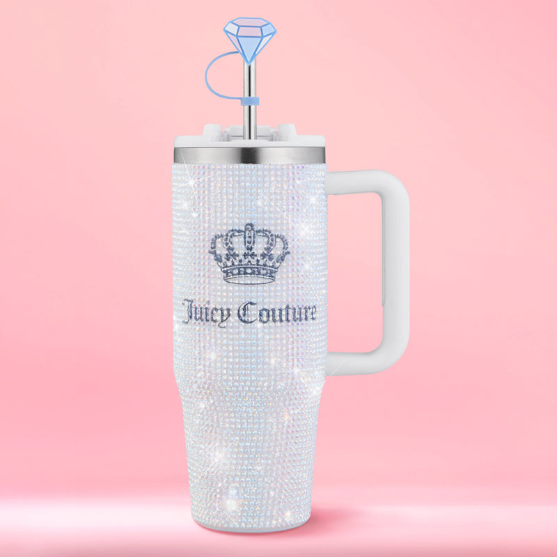 A dazzling Diamond Bling Stainless Steel Tumbler with Handle and Straw, 30 oz, embellished with sparkling rhinestones, a crown logo, white handle, and a blue diamond-shaped straw topper is showcased against a pink background. This glamorous tumbler elevates your everyday drinks with its eye-catching design.
