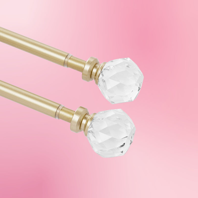 Two Astoria 2-Piece Adjustable Curtain Rod Sets in gold, each featuring faceted clear crystal finials, are displayed on a soft pink gradient background.