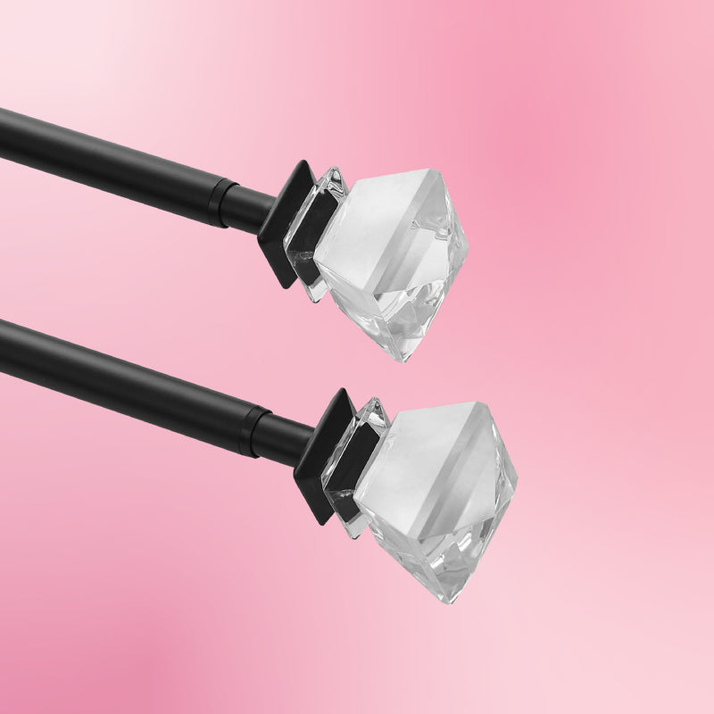 Two Bel Air 2-Piece Adjustable Curtain Rod Sets, featuring black rods with clear faceted crystal finials, are arranged diagonally on a pink background.