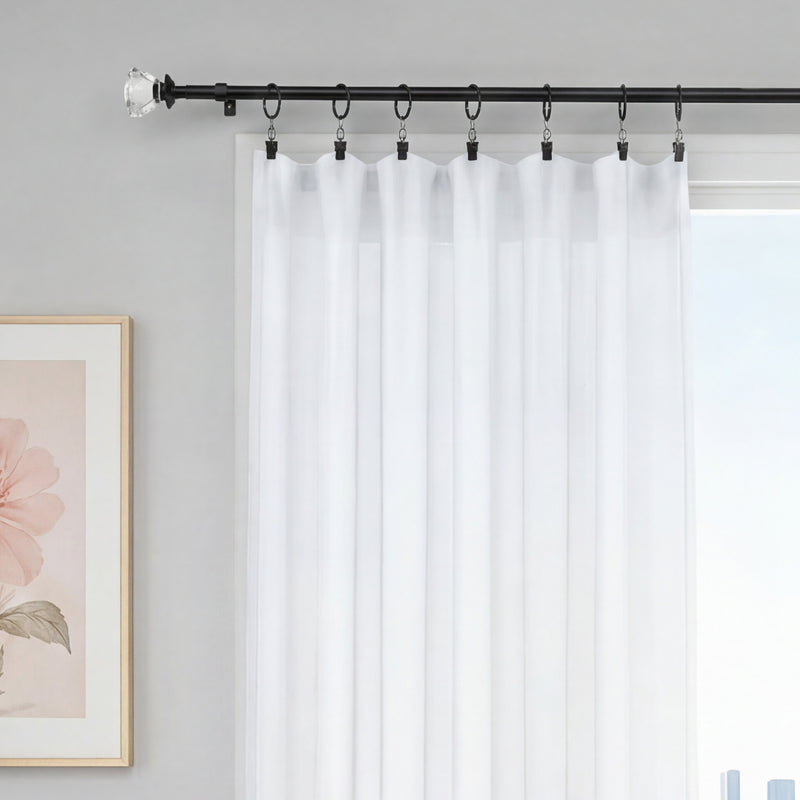A window with sheer white curtains hanging from the Bel Air 2-Piece Adjustable Curtain Rod Set with rings, next to a framed artwork of a pink flower on a light gray wall.