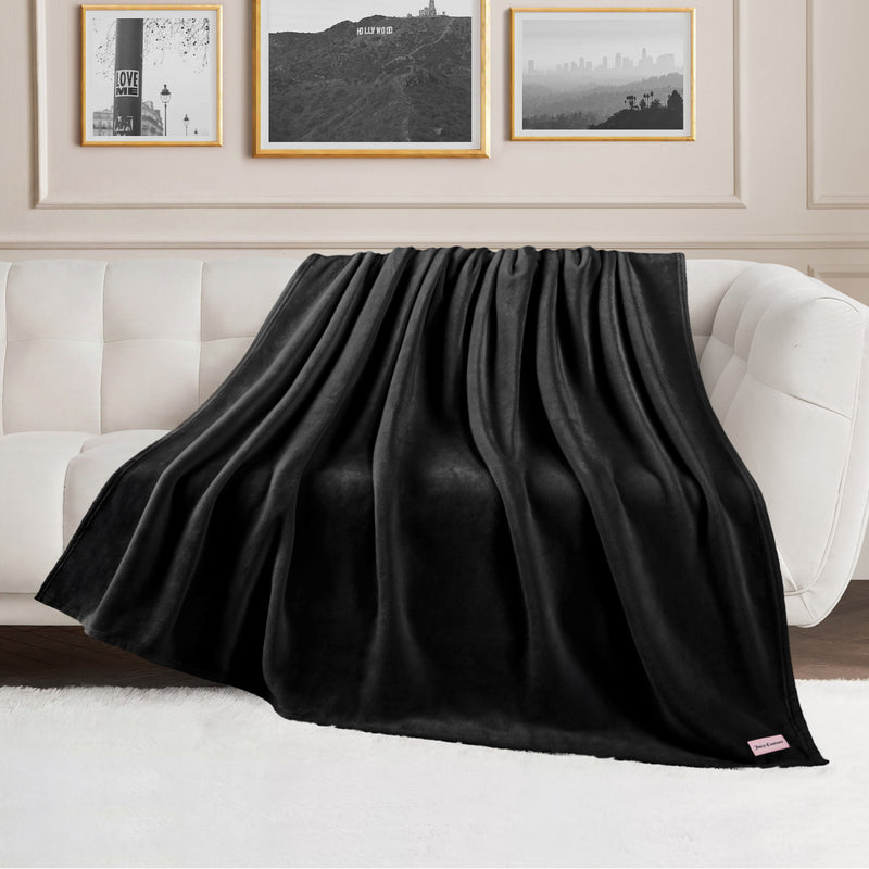 A Plush Oversized Throw Blanket, 60″ x 70″, is draped over a white couch in a modern living room with framed wall art and a fluffy white rug, adding an ultra-soft touch to the cozy space.