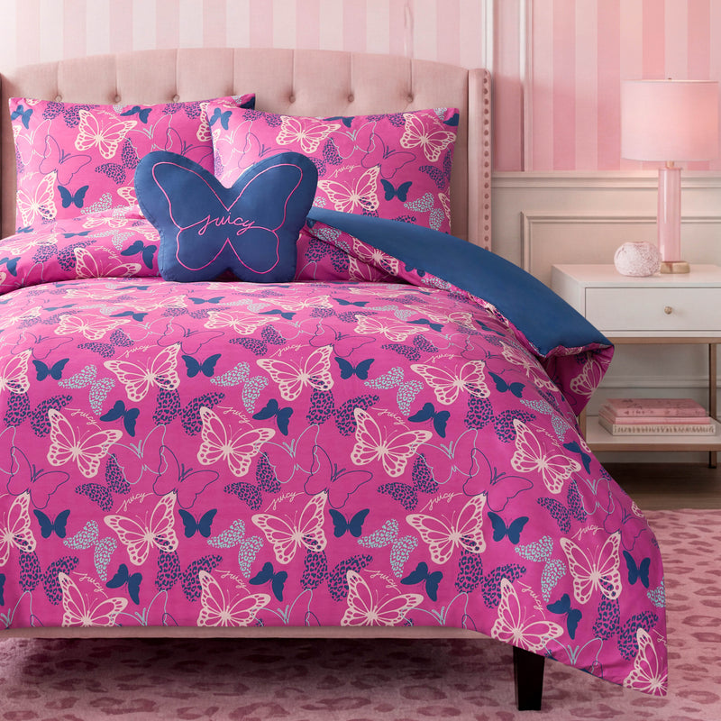 A bed styled with the Kids Wild Butterfly Toss Reversible Comforter Set features a pink butterfly-themed comforter with blue accents, coordinating pillows, and a decorative butterfly accent pillow in front. Complemented by pink striped walls, a nightstand, lamp, and a pink rug, this setup adds playful charm to any kids bedding ensemble.