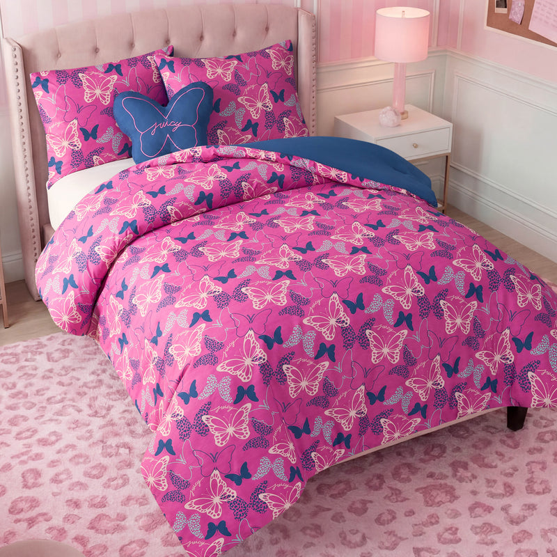 A neatly made bed with the Kids Wild Butterfly Toss Reversible Comforter Set in pink and purple, matching shams, and a decorative blue butterfly pillow. The room features stylish kids’ bedding accents such as a pink lamp, white furniture, and a pink leopard-print rug.