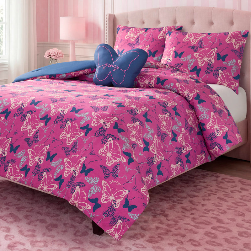 A bed featuring the Kids Wild Butterfly Toss Reversible Comforter Set, matching pillowcases, a blue butterfly-shaped pillow, and a tufted pink headboard creates the perfect kids bedding ensemble in this charming pink, striped bedroom.