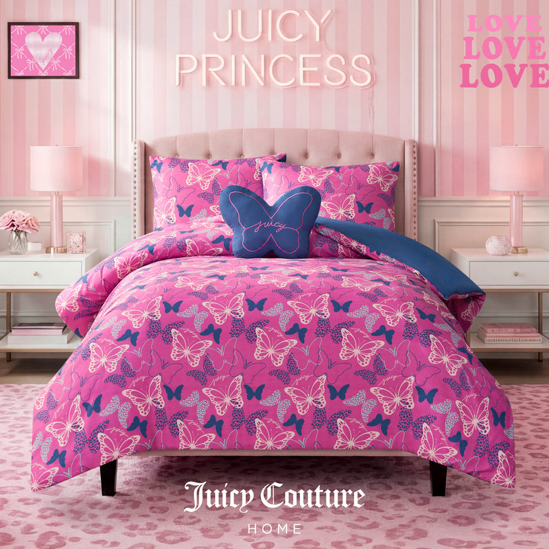 A pink bedroom featuring a bed made up with the Kids Wild Butterfly Toss Reversible Comforter Set, complemented by a butterfly pillow, striped pink walls, framed butterfly art, and “JUICY PRINCESS” text above the bed.