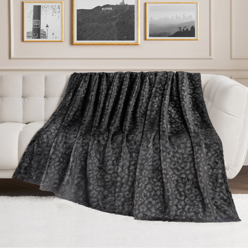 An Embossed Plush Oversized Throw Blanket in dark gray leopard print draped over a white tufted sofa in a living room with framed wall art and a white rug adds an extra touch of luxury and style.
