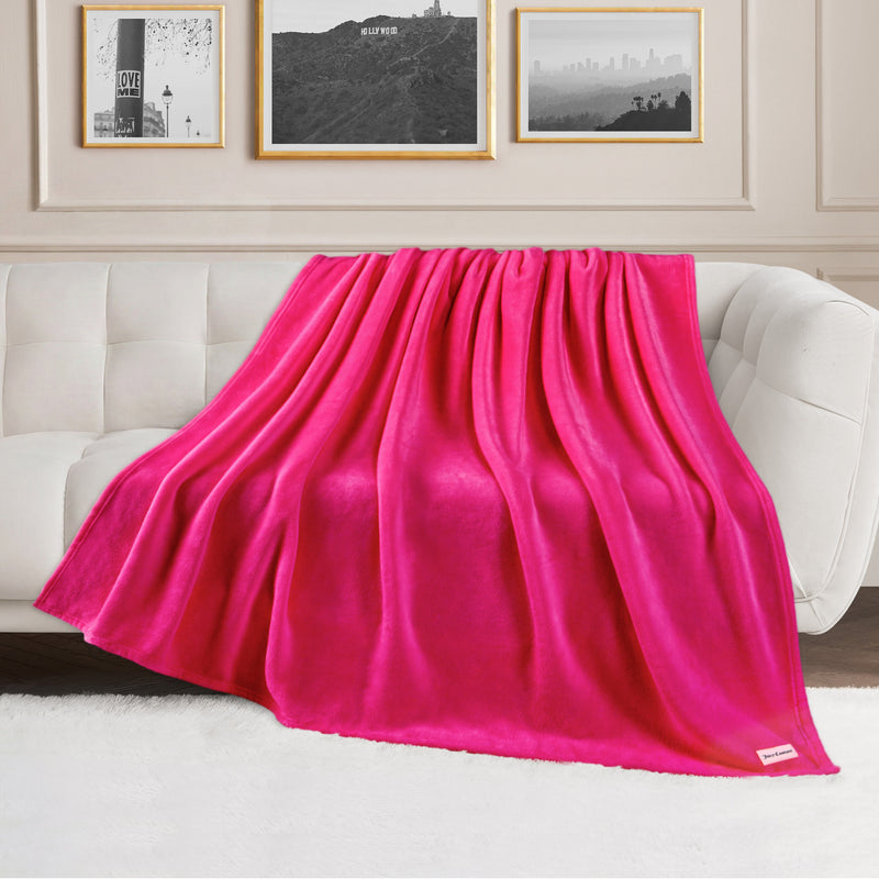 A Plush Oversized Throw Blanket, 60″ x 70″, in bright pink is draped over a white sofa in a living room with framed pictures on the wall and a white rug on the floor.