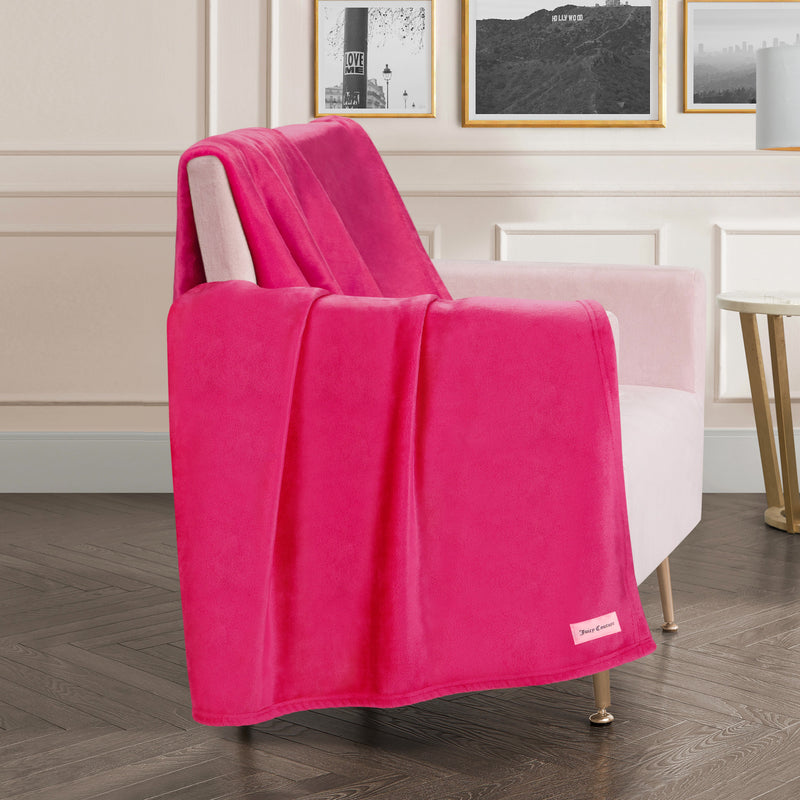 A Plush Oversized Throw Blanket, 60″ x 70″, in bright pink is draped over a light pink armchair in a stylish living room with framed art on the wall and a gold side table nearby.
