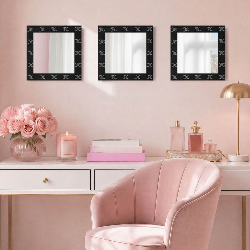 A pink vanity area featuring a blush chair, white desk, pink roses, a candle, perfumes, and the Velour Rhinestone Logo 3-Piece Decorative Mirror Set—three square mirrors with velour-look frames—displayed on a light pink wall.