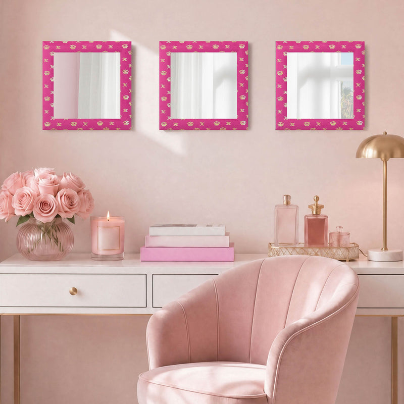 A pink-themed vanity area featuring a blush chair, a white desk, pink roses in a vase, a candle, and the Velour Crown Foil Print Hot Pink with Gold Foil 3-Piece 12 in x 12 in Decorative Mirror Set on the wall. The decor is elegant and feminine.