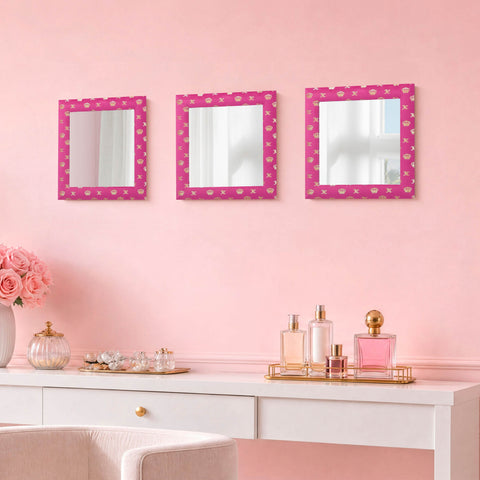 A vanity adorned with a white desk, pink perfume bottles, pink roses in a vase, and the Velour Crown Foil Print Hot Pink with Gold Foil 3-Piece 12 in x 12 in Decorative Mirror Set against a pale pink wall creates an elegant and charming atmosphere. Each mirror is ready-to-hang, allowing you to effortlessly enhance your room with graceful style.