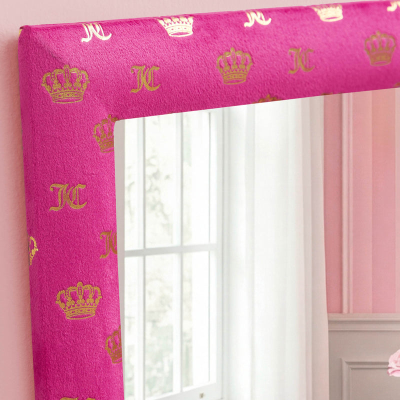 A close-up of the Velour Crown Foil Print Hot Pink with Gold Foil 3-Piece 12 in x 12 in Decorative Mirror Set shows its pink velour-look frame adorned with gold crowns and KC letters, reflecting a window and a glimpse of a pink-walled room. This ready-to-hang mirror set brings a charming accent to any space.