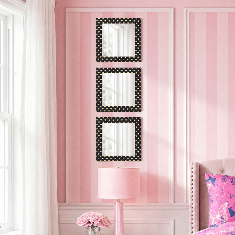 A charming trio from the Velour Heart Foil Print 3-Piece Decorative Mirror Set, each rectangular mirror featuring velvety frames adorned with black and white polka dots, hangs vertically on a pink striped wall above a lamp and a vase of pink roses. Situated near a window framed by white curtains and beside a bed topped with a pink pillow, this stylish wall décor brings playful elegance to the room.
