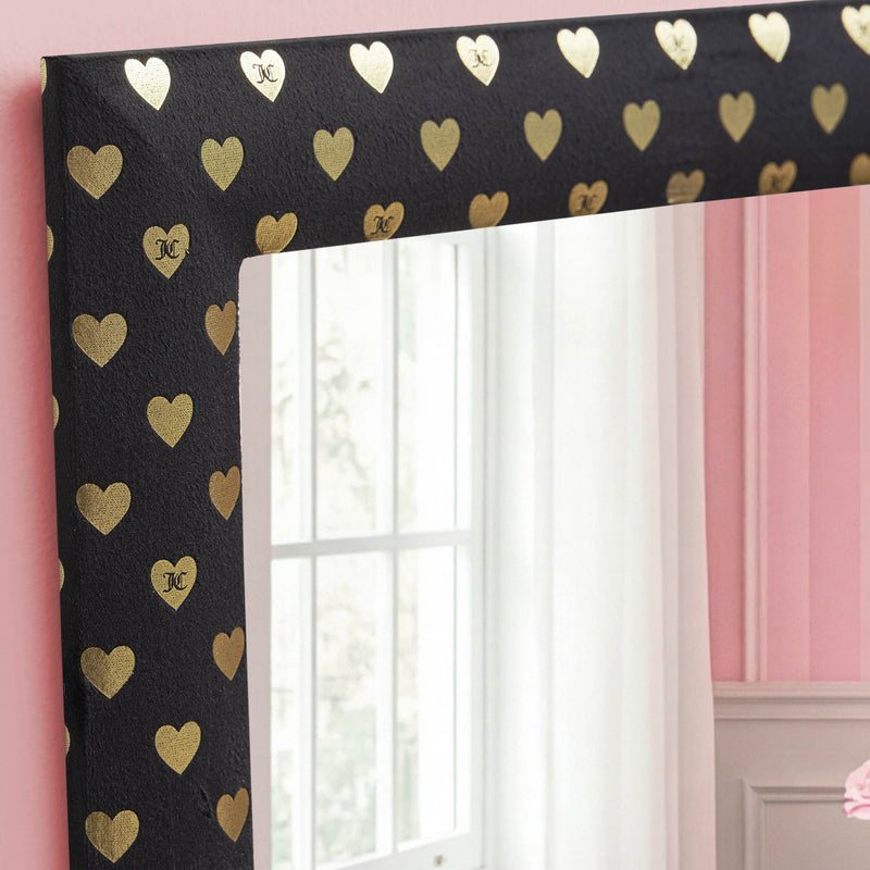 The Velour Heart Foil Print 3-Piece Decorative Mirror Set features black, velour-look frames accented with gold heart designs, each displaying a small “KC.” These mirrors reflect elements of a pink and white room and a window, adding an elegant touch to any wall décor.