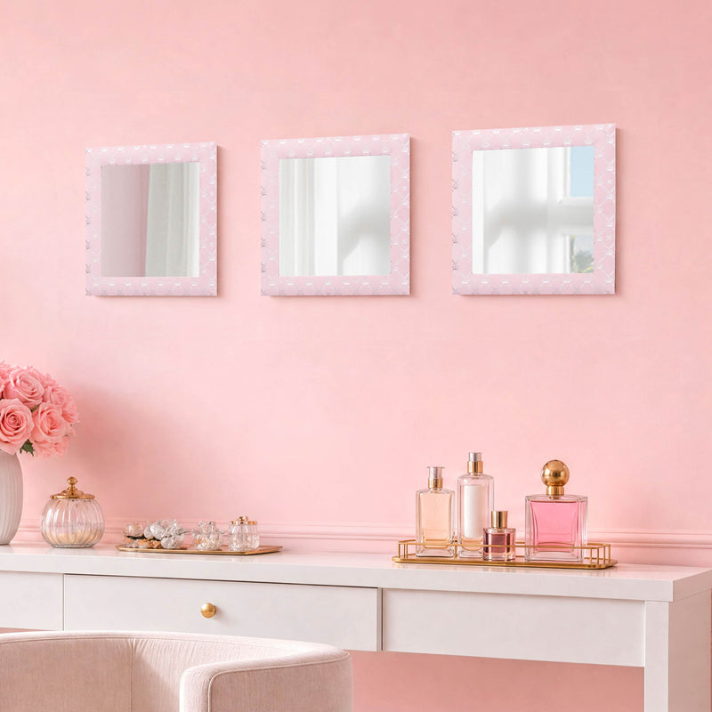 A vanity table with perfume bottles, a vase of pink roses, and glass containers sits against a pink wall adorned with the Velour Lattice Crown Foil Print 3-Piece Decorative Mirror Set arranged above it.