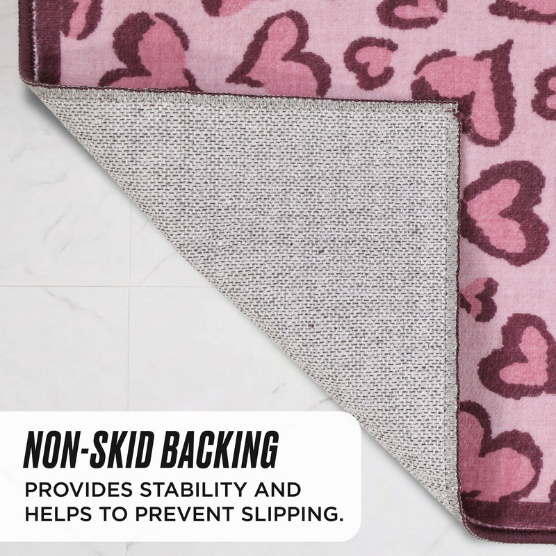 The Finley Washable Rug, 2′ x 4′ is an ultra-soft, pink Juicy Couture rug with a heart pattern, shown corner-folded to reveal the textured non-skid backing.