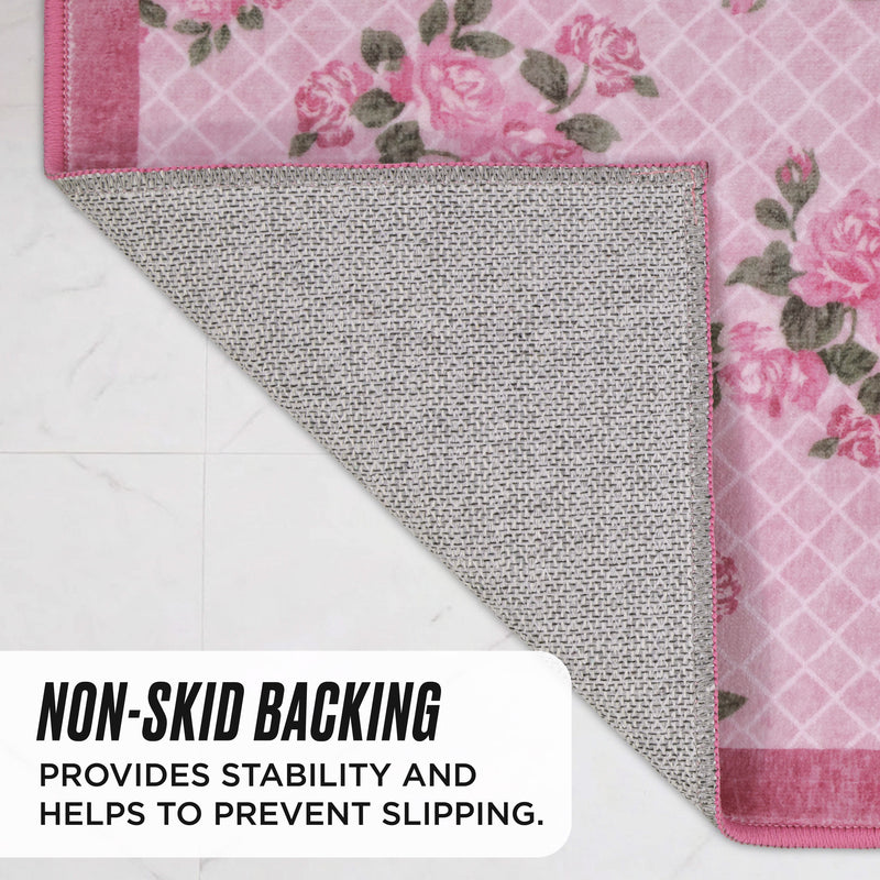 Finley Washable Rug, 2′ x 4′ in pink with a rose pattern and white grid overlay, shown with one corner folded up to reveal a gray textured non-skid backing.