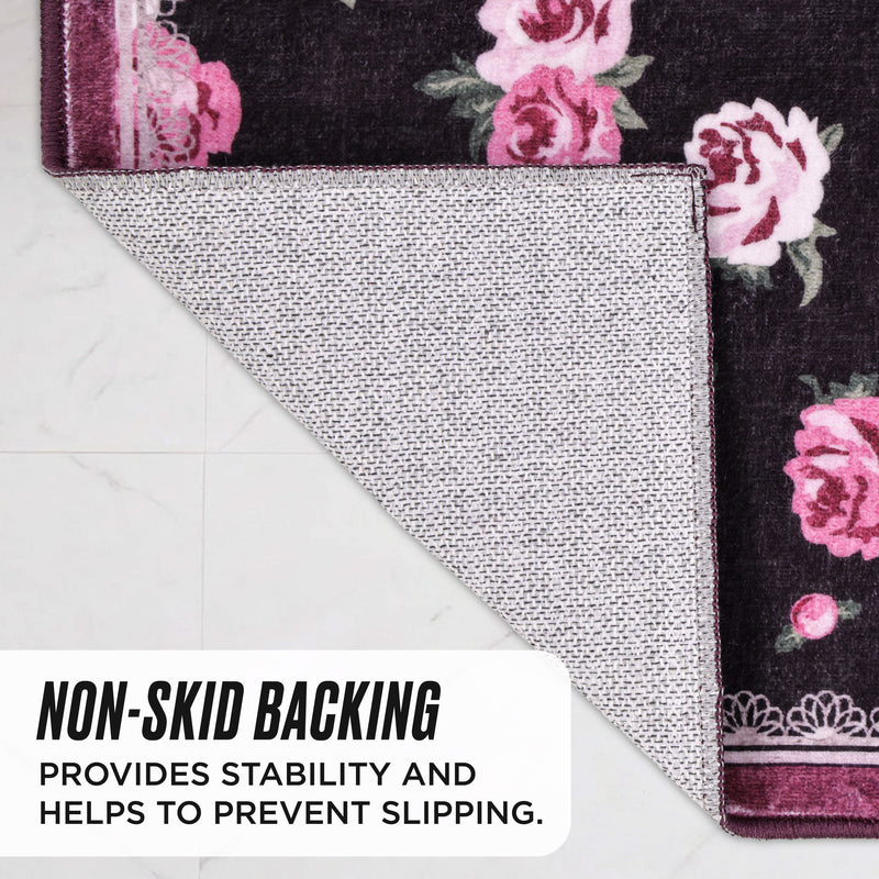 The Finley Washable Rug, 2′ x 4′, is a rectangular, ultra-soft rug with a dark floral pattern, folded to show its textured, non-skid backing that provides stability and prevents slipping.