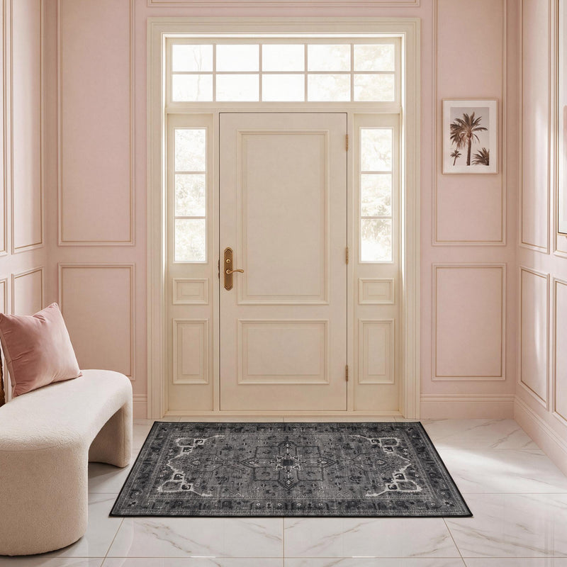 The Finley Washable Rug, 2′ x 4′, is an ultra-soft, machine-washable rug with a grey and black ornate medallion pattern laid on a white marble floor in an entryway.