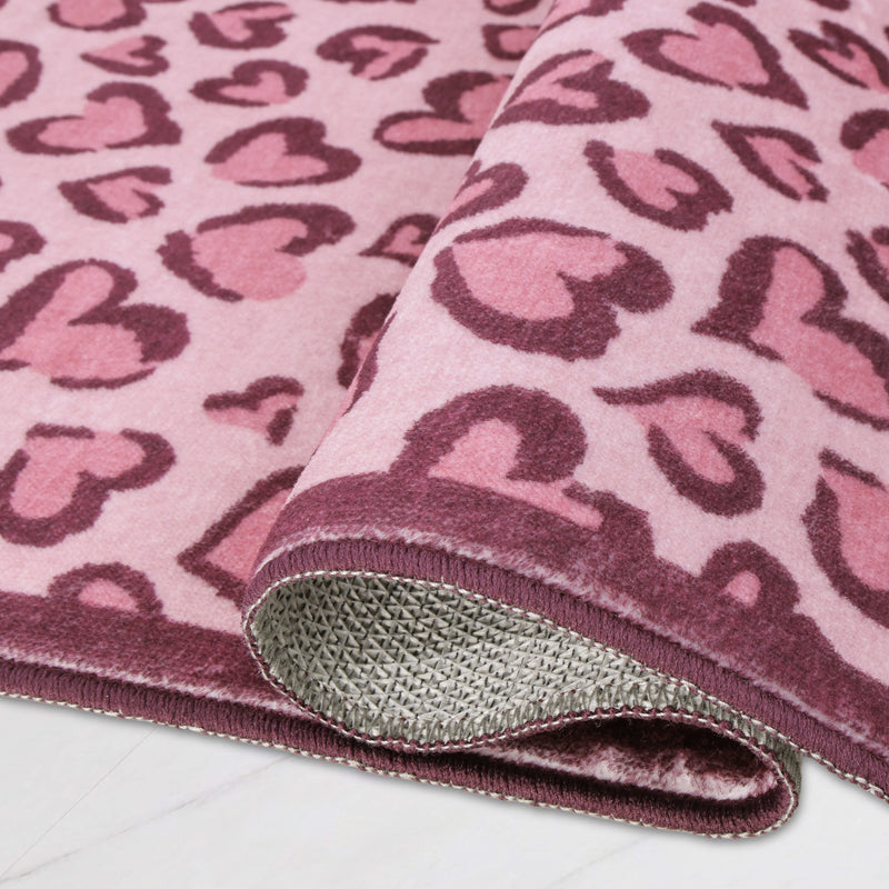Finley Washable Rug, 2′ x 6′, an ultra-soft runner rug with a pink and dark red leopard-print heart pattern, shown partially rolled to reveal the textured underside.
