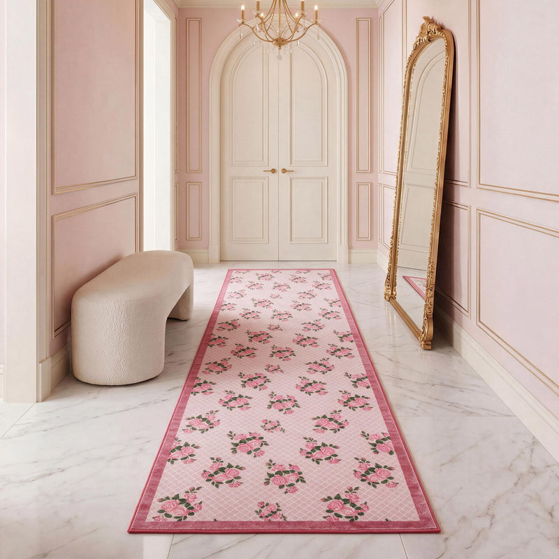 A rectangular, ultra-soft Finley Washable Rug, 2′ x 6′ with a pink grid pattern and repeating rose bouquets, centered on a marble floor in a pink hallway.