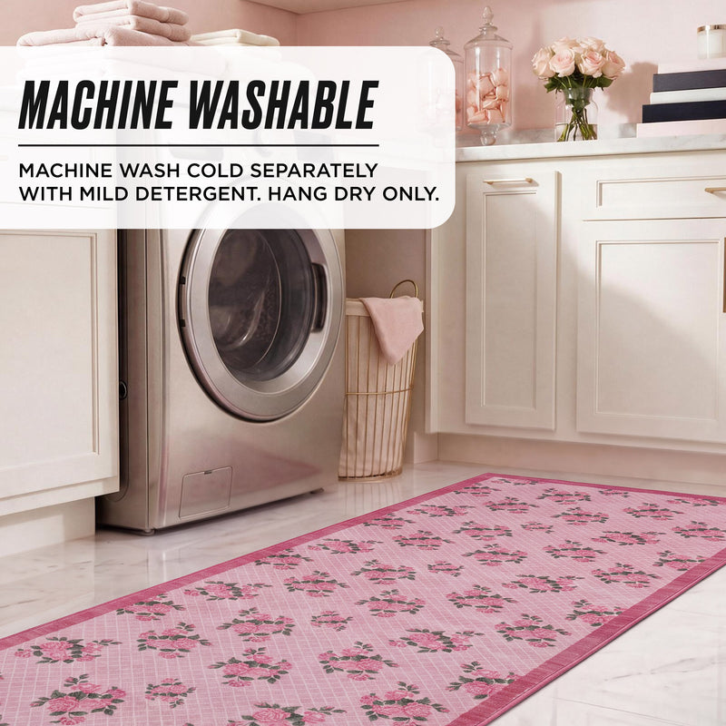 A rectangular pink floral Finley Washable Rug, 2′ x 6′ laid on a laundry room floor in front of a washing machine, overlaid with text stating the ultra-soft rug is machine washable and providing care instructions.