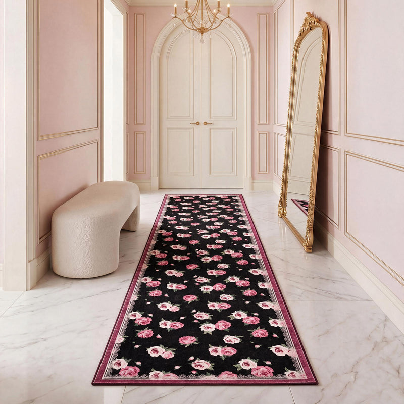 A Finley Washable Rug, 2′ x 6′ rectangular runner with an ultra-soft black background featuring a repeating pattern of pink roses and lace-like borders, placed in a hallway.
