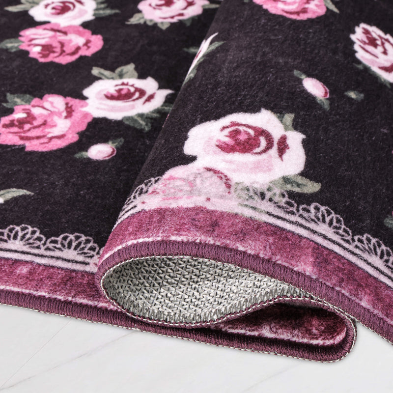 Finley Washable Rug, 2′ x 6′, an ultra-soft runner with a dark purple background and pink rose pattern, partially rolled to show the underside.