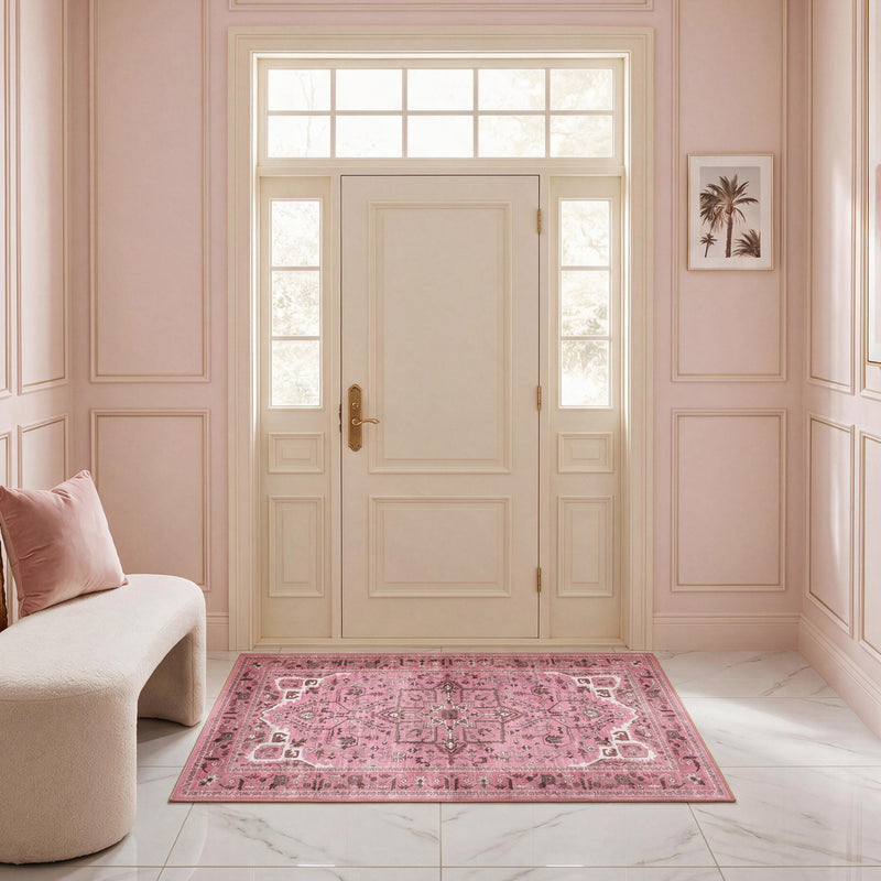 A Finley Washable Rug, 2′ x 4′, ultra-soft, rectangular, and pink with a traditional ornate pattern, centered on a white marble floor in a foyer.