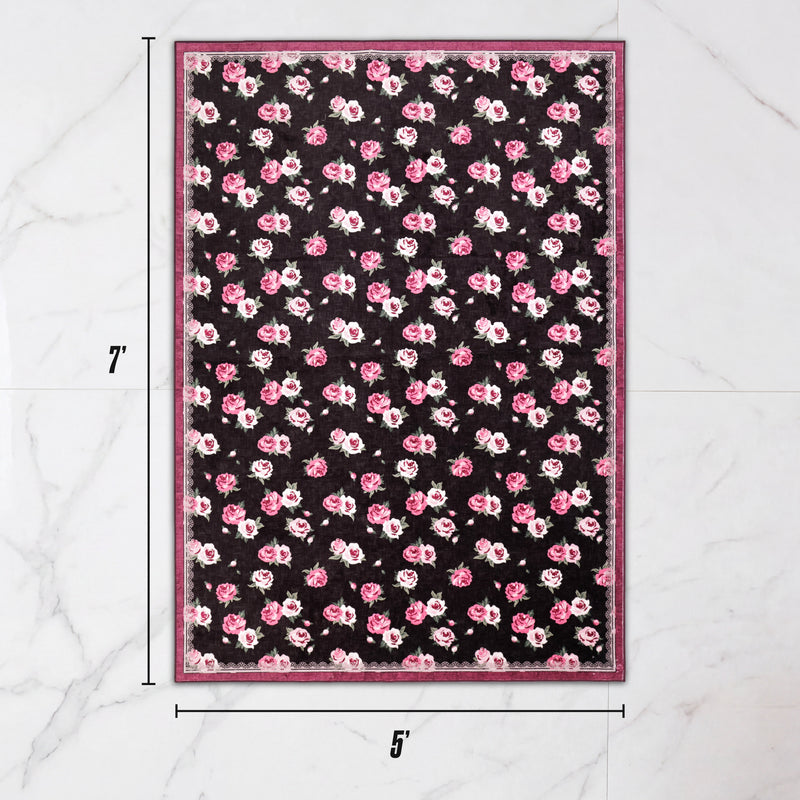 Finley Washable Rug, 5′ x 7′, is an ultra-soft, rectangular rug featuring a repeating pattern of pink roses on a black background, framed by a patterned magenta border.