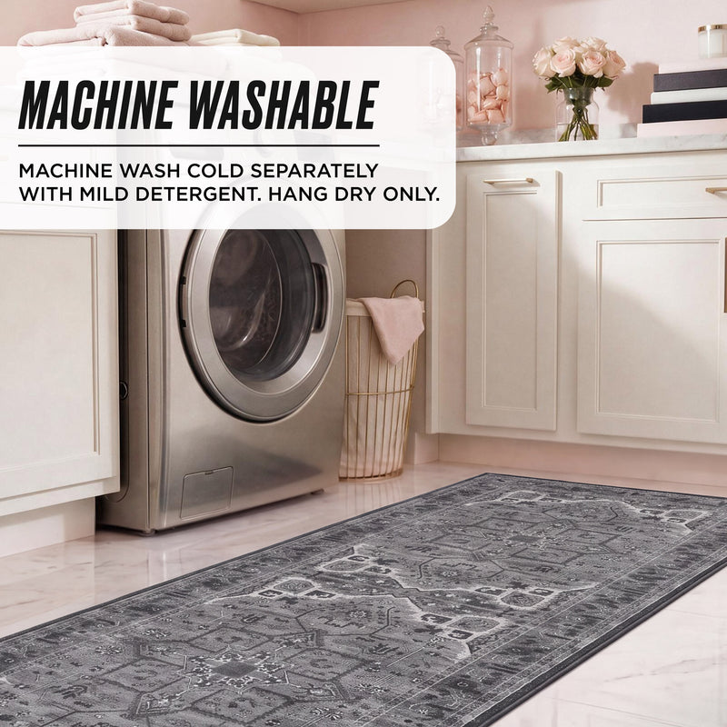 A gray, machine-washable Finley Washable Rug, 2′ x 6′ with a vintage-inspired pattern lies on a kitchen floor in front of a washing machine; an overlay reads Machine Washable: Machine wash cold separately with mild detergent. Hang dry only.