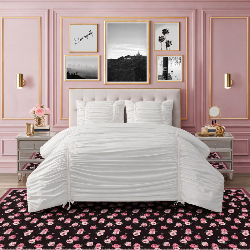 Finley Washable Rug, 8′ x 10′ in an ultra-soft, machine-washable style featuring a black background and a repeating pattern of pink roses, displayed in a bedroom with a white tufted bed and pink paneled walls.