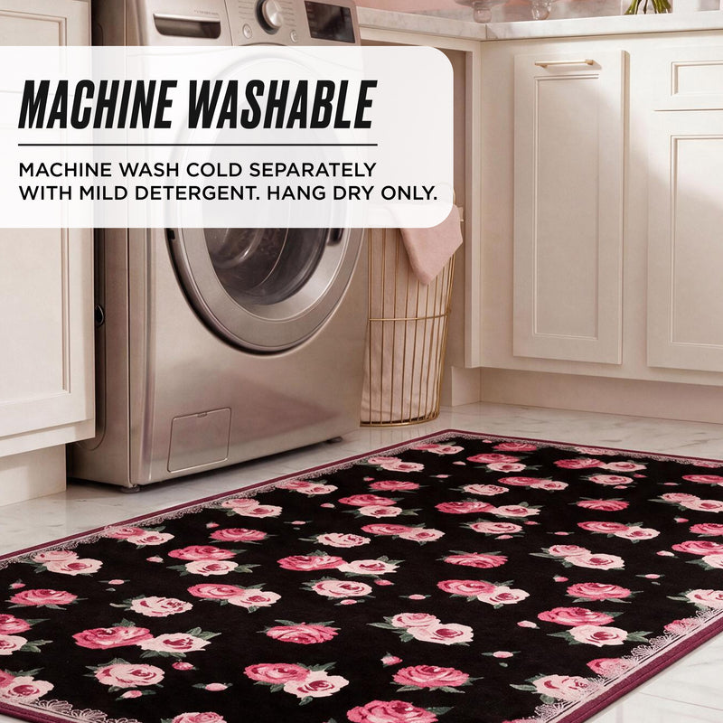 Finley Washable Rug, 8′ x 10′, featuring a black rectangular design with a pink rose floral pattern, placed in a laundry room in front of a washing machine with care instructions printed on the rug.