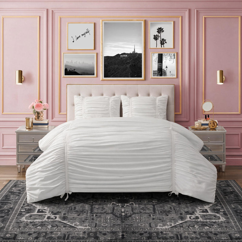 A Finley Washable Rug, 5′ x 7′, in ultra-soft dark gray with a vintage-inspired floral pattern lies beneath a bed with a white ruched comforter in a room with pink paneled walls.
