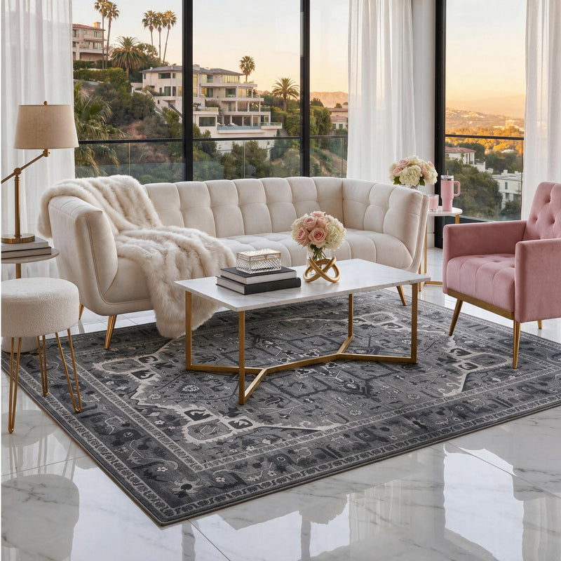 The Finley Washable Rug, 5′ x 7′, is an ultra-soft, machine-washable rectangular area rug in shades of gray with a traditional ornate pattern, centered in a living room under a white coffee table.