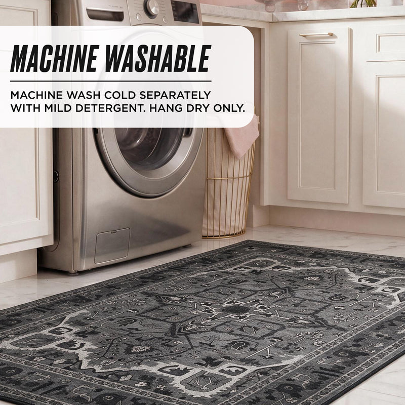 A grey, rectangular Finley Washable Rug, 8′ x 10′ with a distressed floral pattern on a kitchen floor in front of a washing machine, featuring text overlay with care instructions: MACHINE WASHABLE. MACHINE WASH COLD SEPARATELY. HANG DRY ONLY.