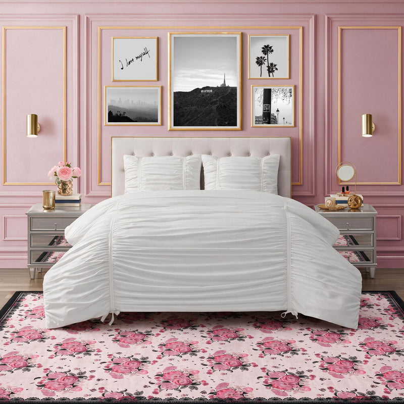 An ultra-soft Finley Washable Rug, 8′ x 10′, featuring a repeating pattern of pink and red roses on a light background, positioned beneath a bed in a pink bedroom.