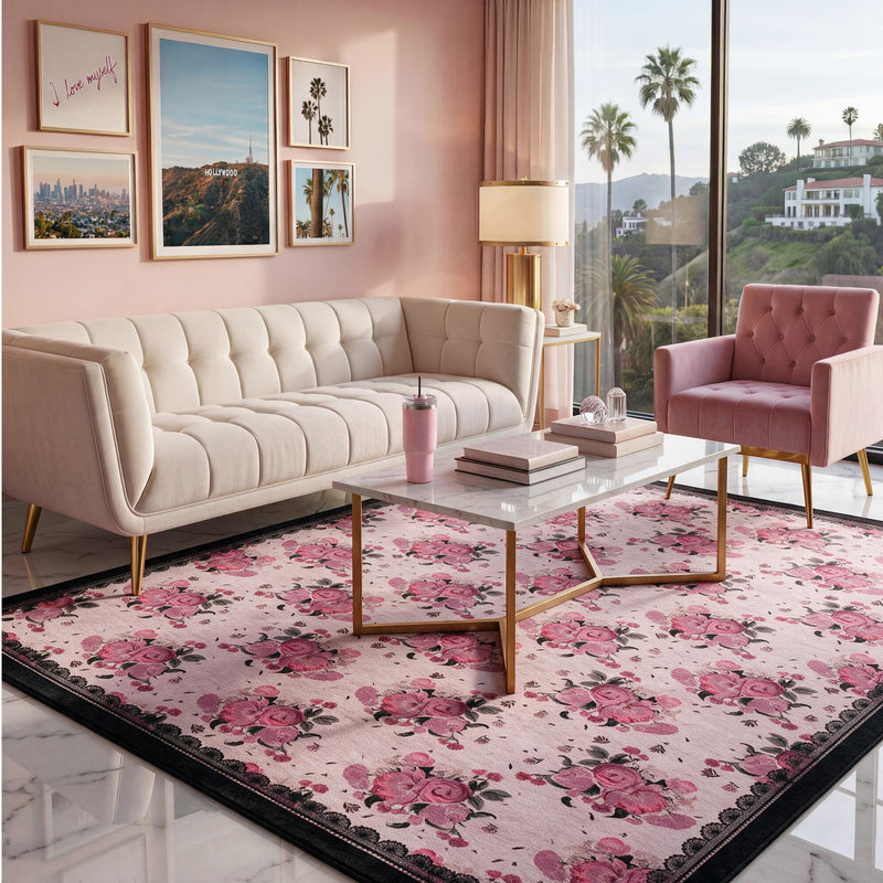 Finley Washable Rug, 8′ x 10′, an ultra-soft rectangular area rug with a pink floral pattern and a wide black border, centered in a living room with a beige sofa, pink armchair, and marble coffee table.