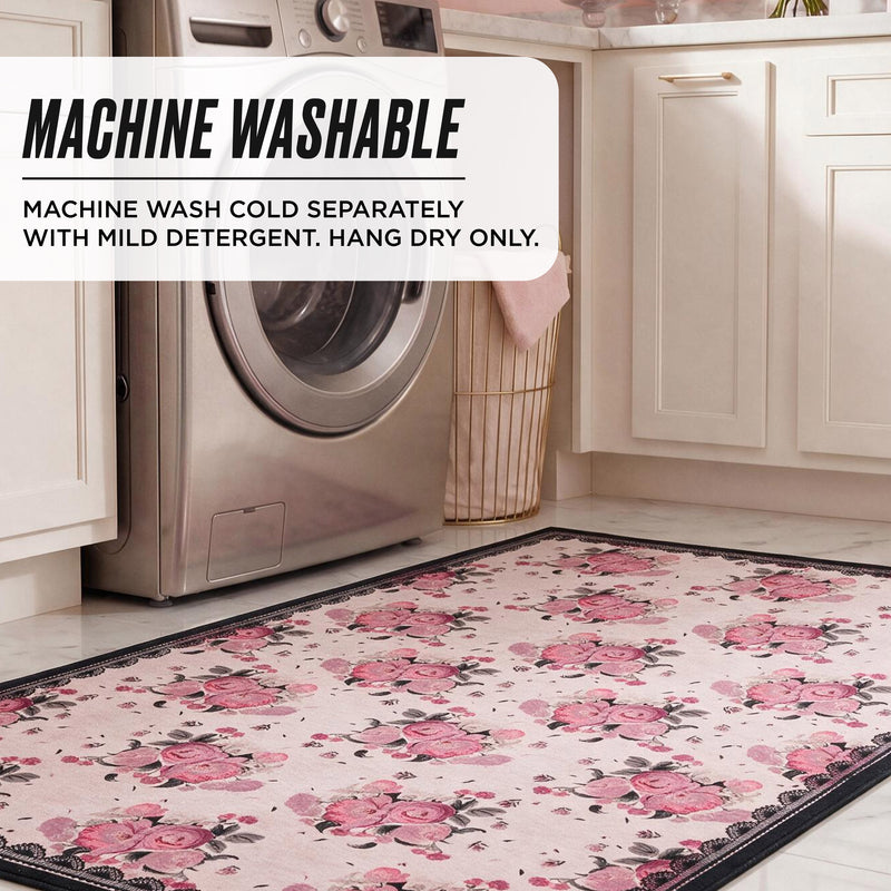 Finley Washable Rug, 8′ x 10′, a rectangular machine-washable rug with a pink floral pattern and a dark border, shown in a laundry room with care instructions: MACHINE WASH COLD SEPARATELY WITH MILD DETERGENT. HANG DRY ONLY.
