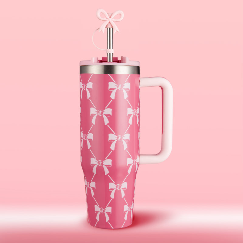 A tall pink Jetsetter Tumbler with Handle, Straw & Topper (30 oz) by Juicy Couture, featuring white bow patterns and a straw adorned with a bow topper, set against a pink background. This stylish travel cup is perfect for keeping your drinks chic and cold wherever you go.