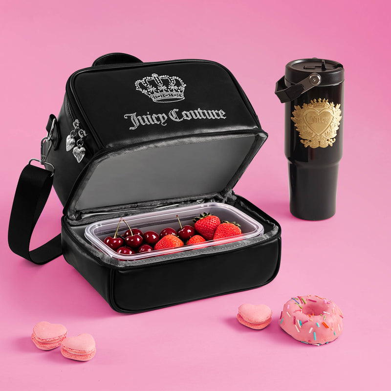 The Double Zip Chill Cooler Bag in black from Juicy Couture, filled with cherries and strawberries, sits next to a sleek black travel mug, three pink macarons, and a pink sprinkle donut—all beautifully arranged on a pink background.